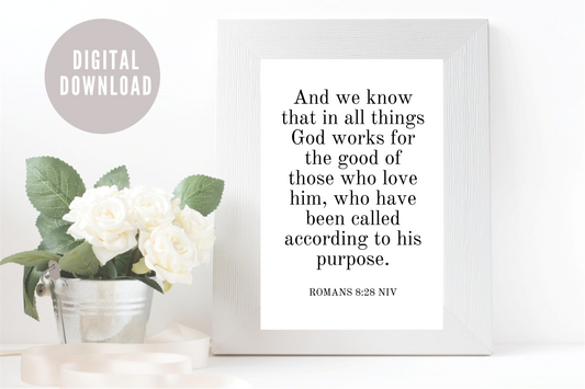Framed print with Romans 8:28 NIV text on a white surface with flowers.