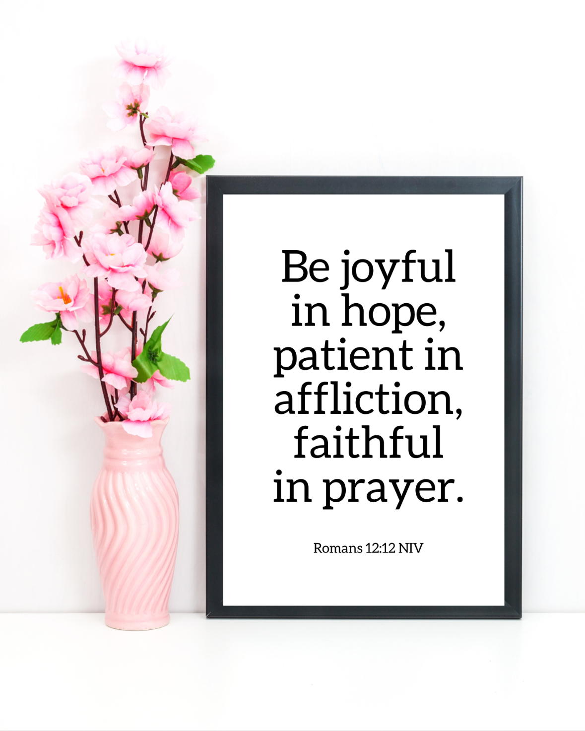 Framed quote 'Be joyful in hope, patient in affliction, faithful in prayer' with pink vase and flowers on white background