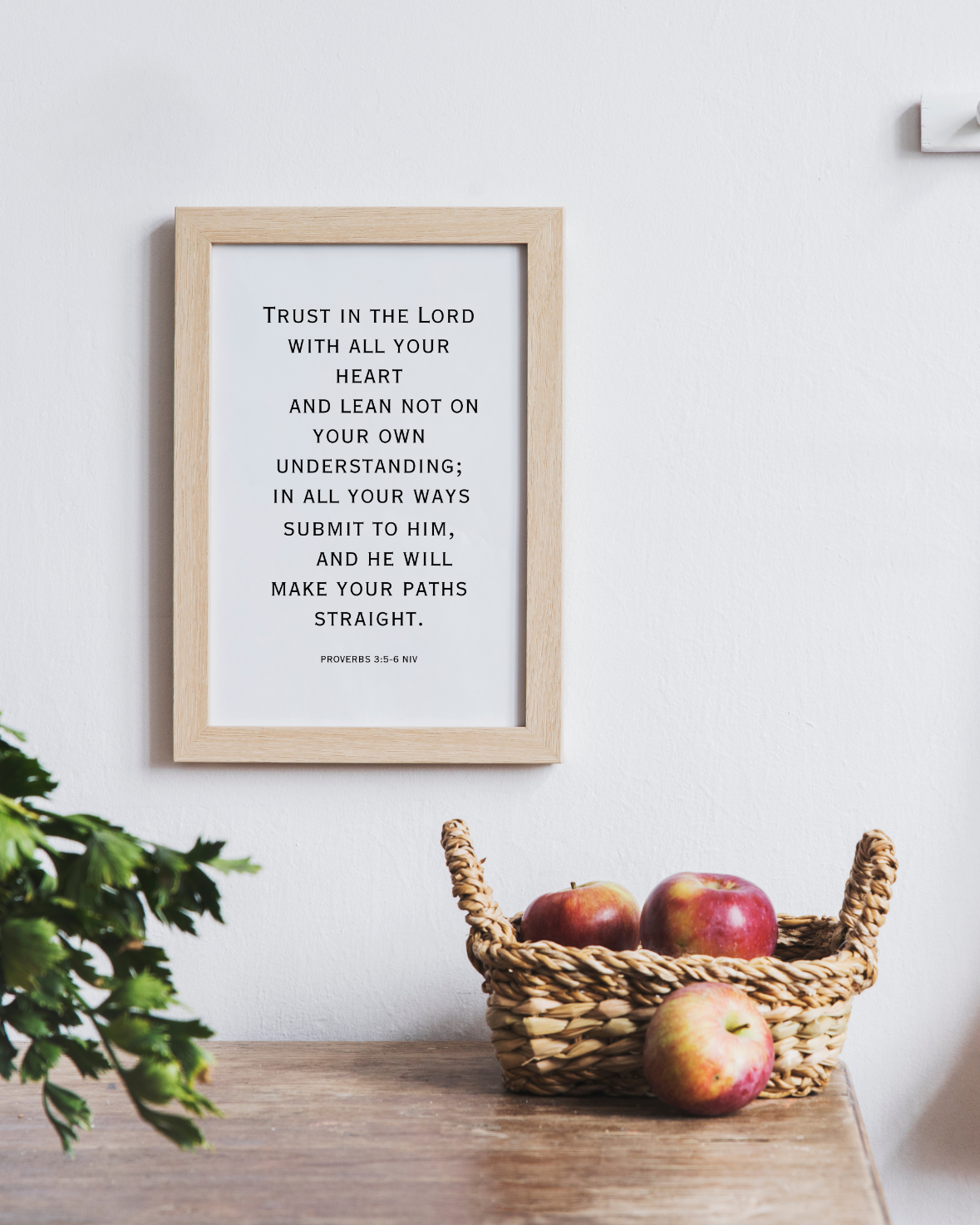 High-definition downloadable wall art featuring Proverbs 3:5 scripture in a contemporary frame on a white wall above a basket of red apples.