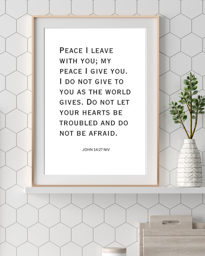 Inspirational Christian quote print of John 14:27 hanging in a contemporary home office with natural lighting and a calm atmosphere.


